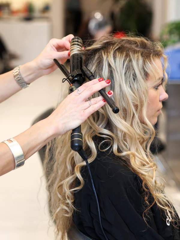 A stylist finishing long blonde curls in the salon chair
